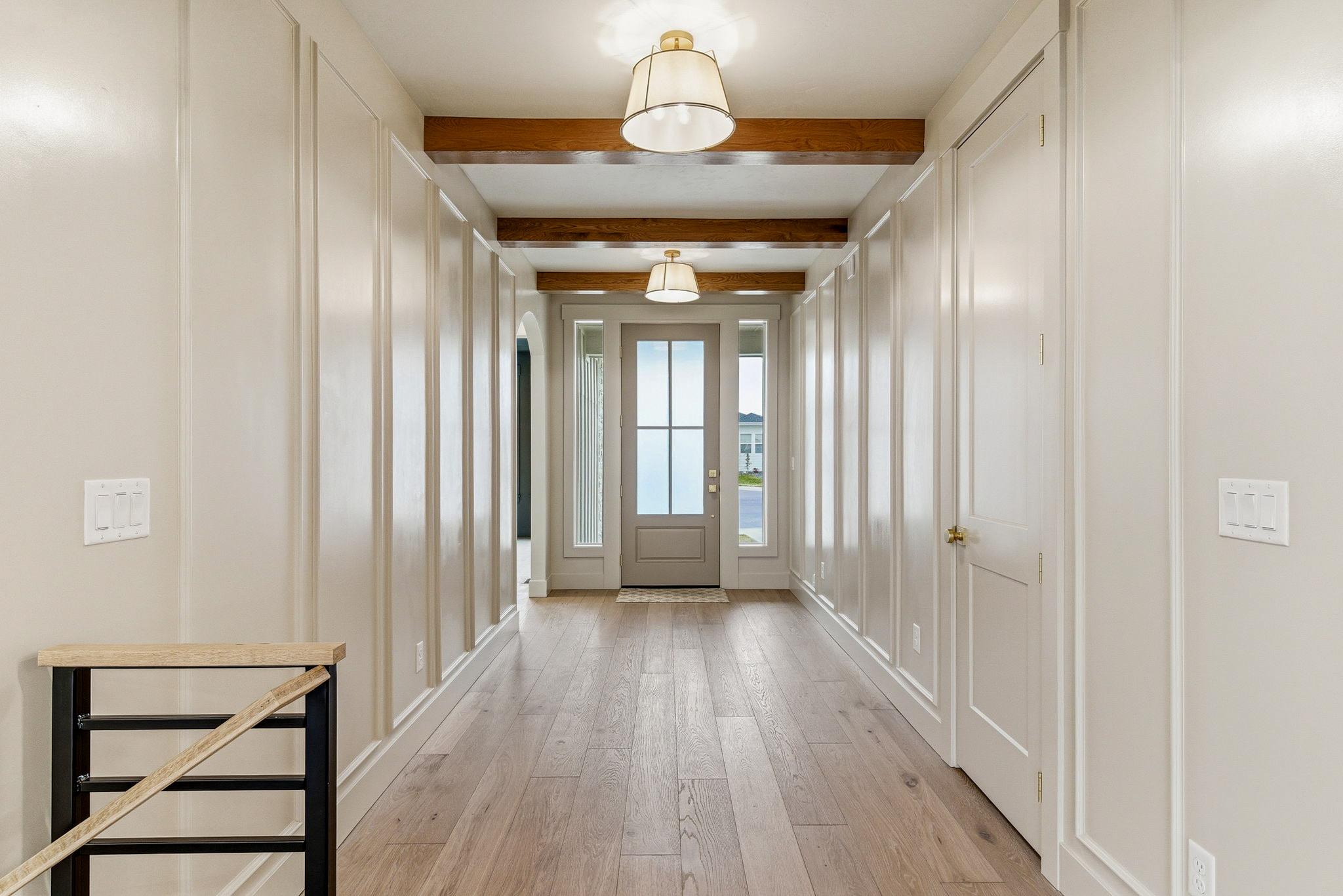 The beamed entry hall with paneled walls, white oak floors, and brass drum lights