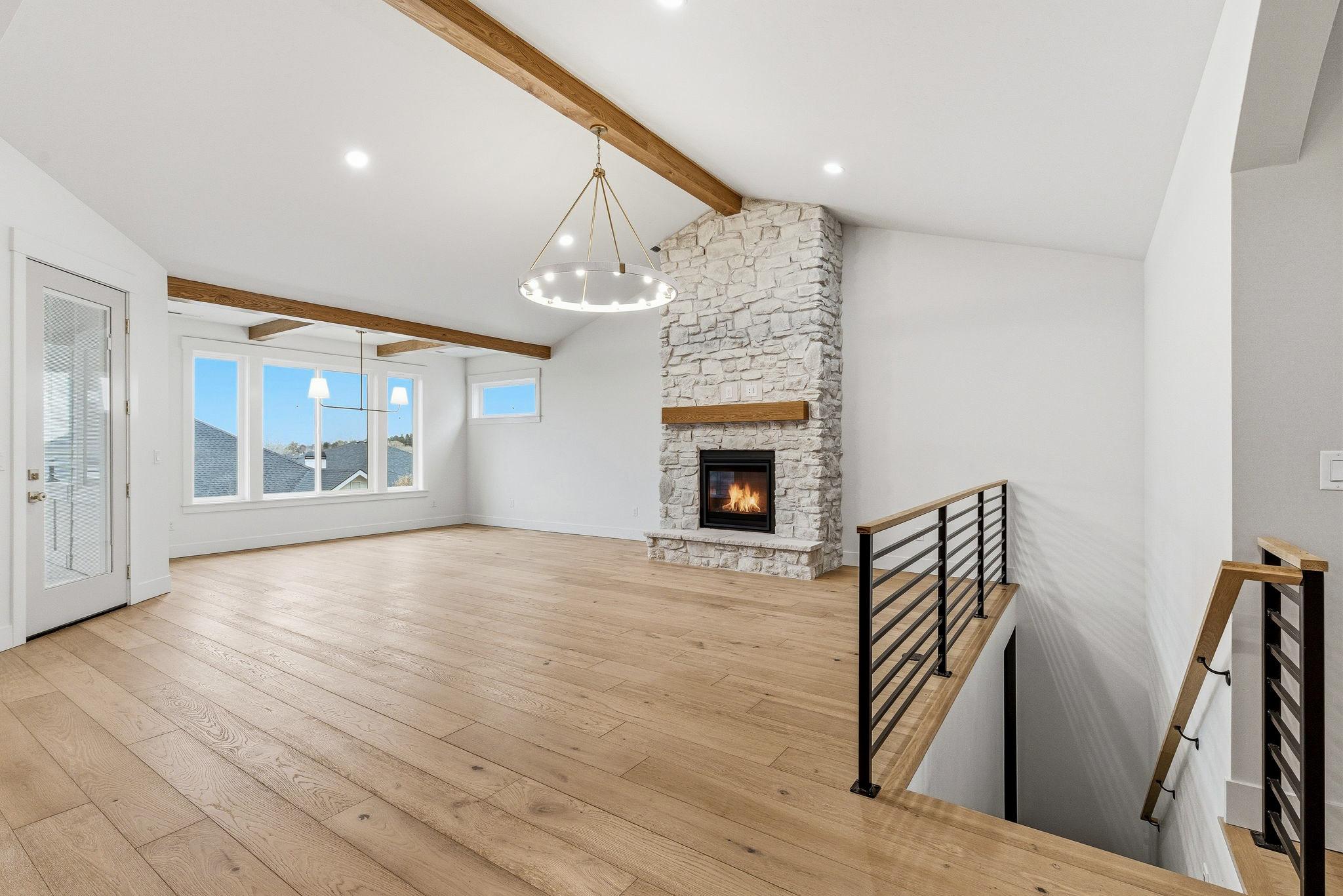 The vaulted great room with wood beams, a floor to ceiling stone fireplace, and a ring chandelier
