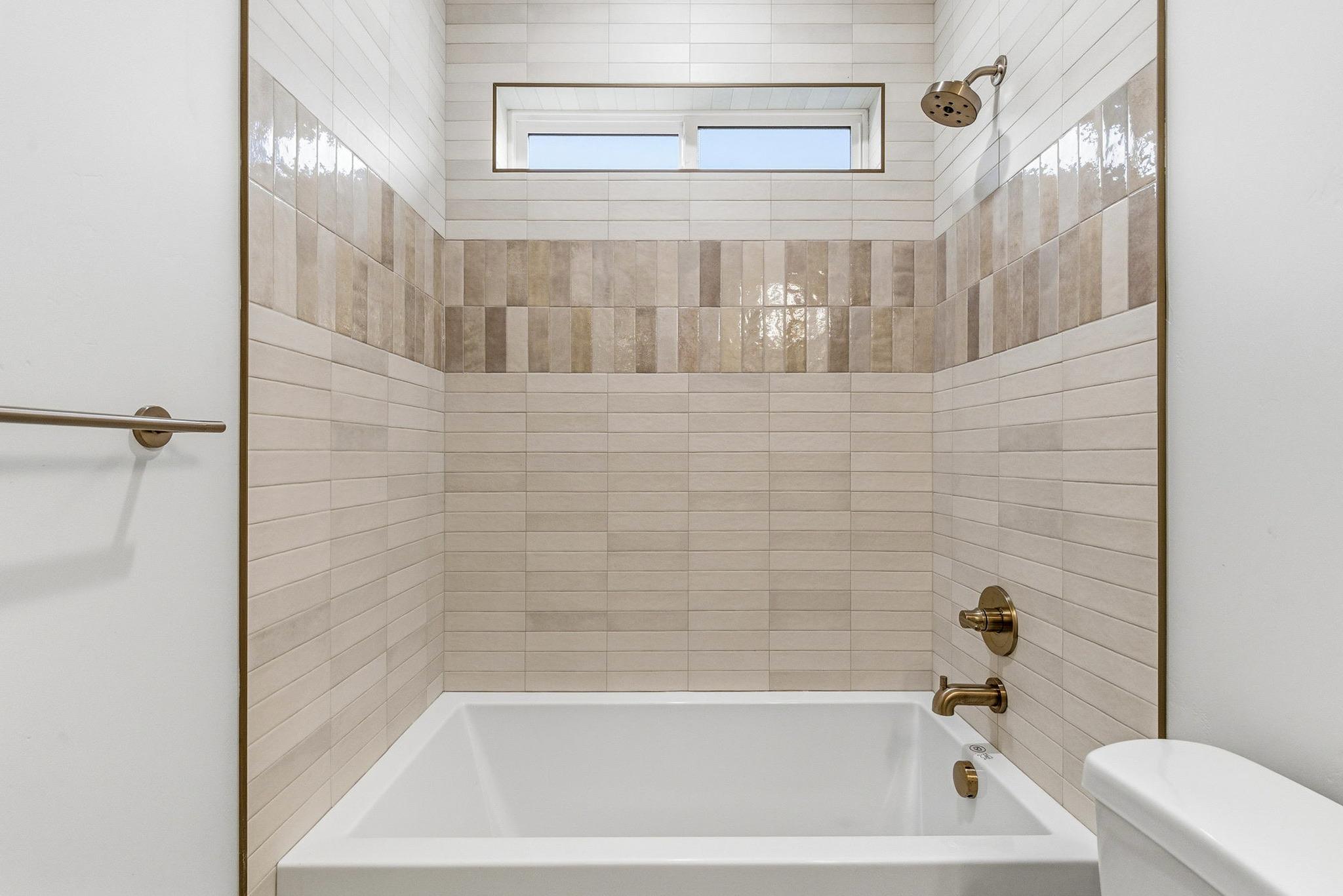 A guest bath with layered tile to the ceiling and brass shower fixtures