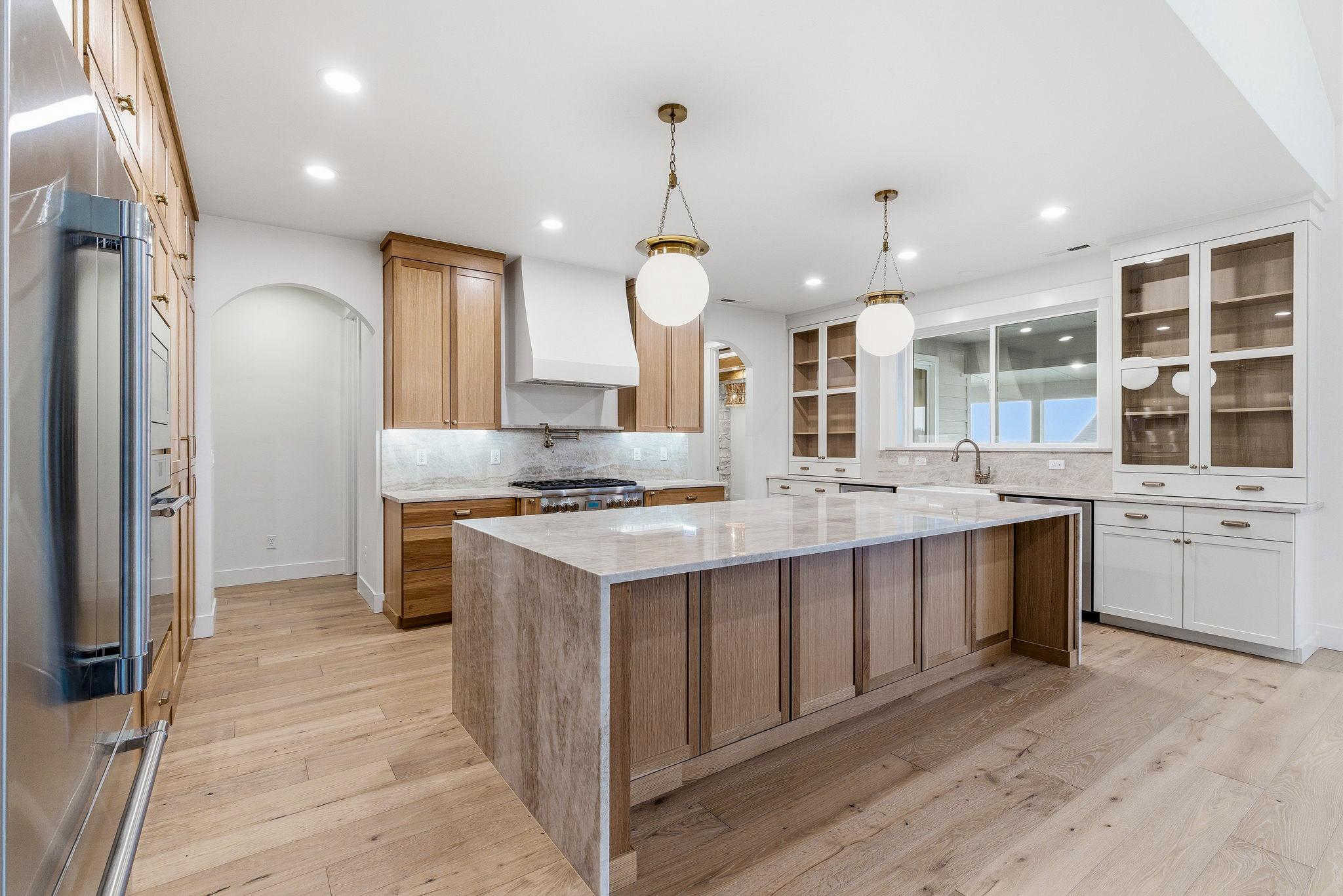 The kitchen: white oak cabinetry, a waterfall stone island, brass globe pendants, and a pot filler over the range