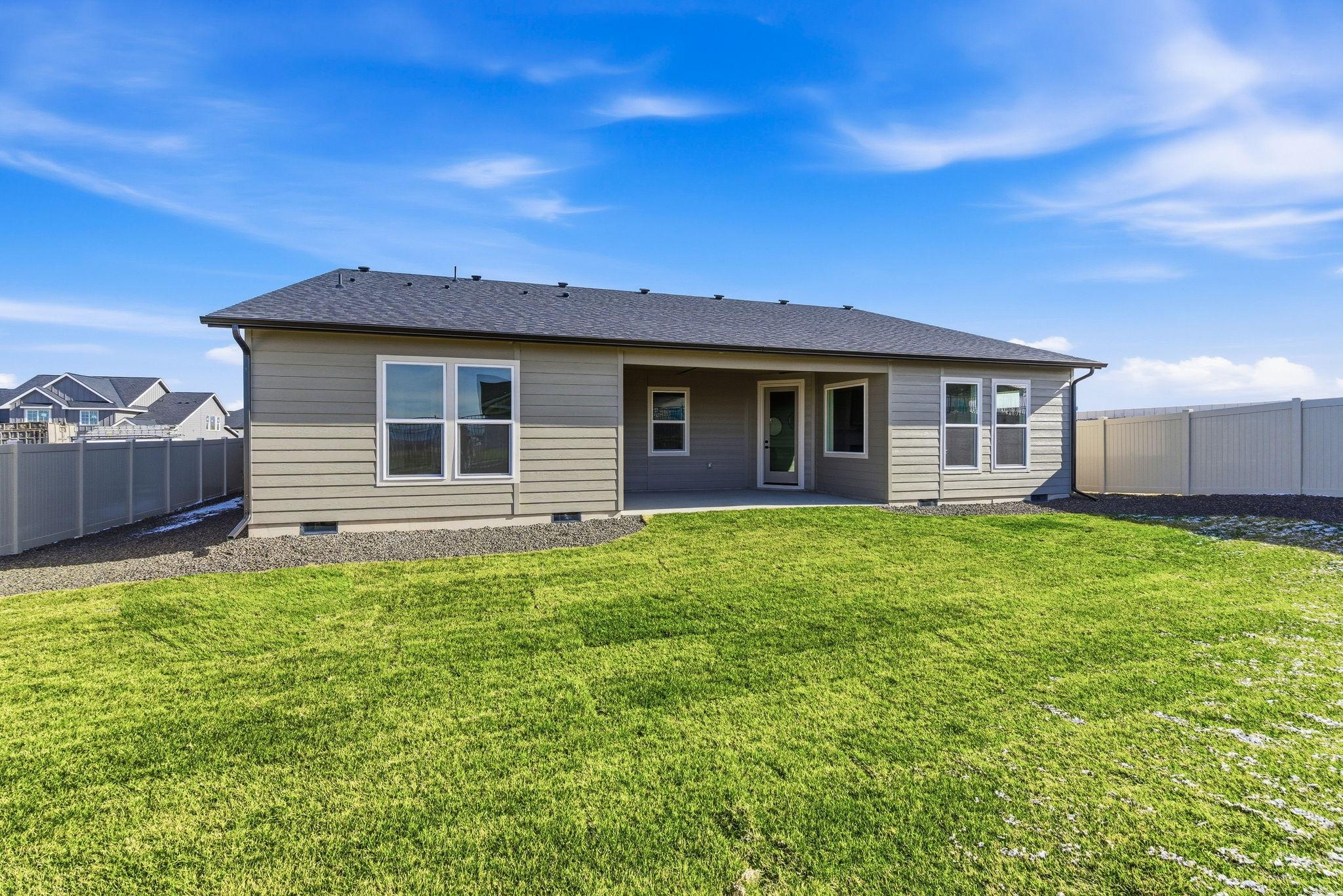 The back of the home: a covered patio running the length of the living space onto a fenced lawn