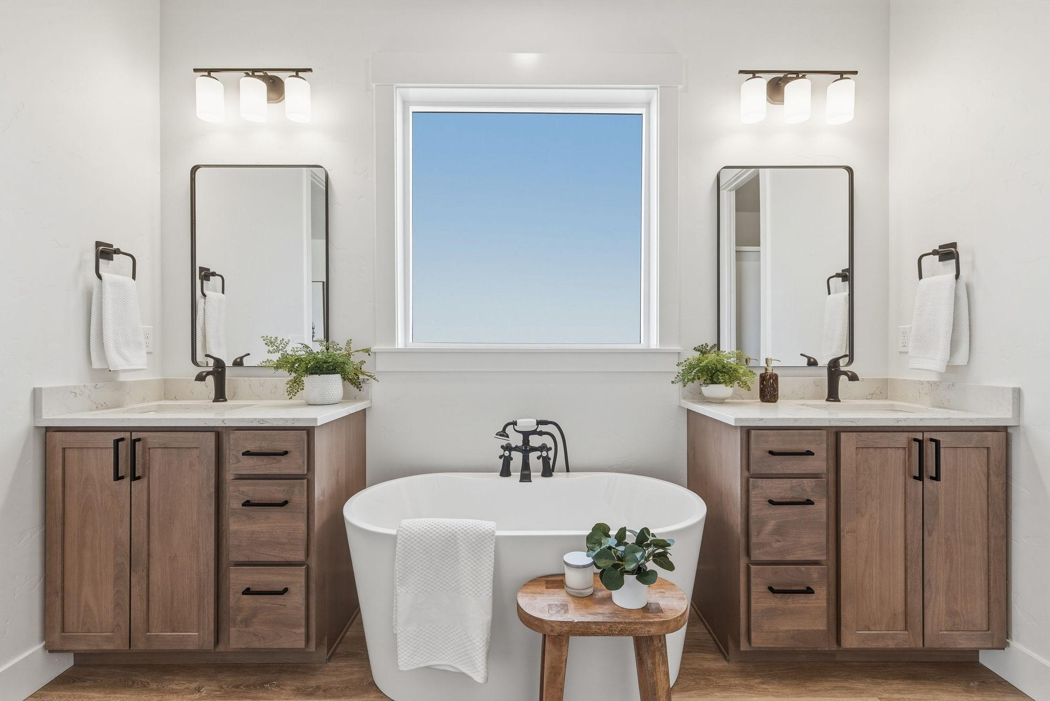The primary bath: dual vanities under bronze sconces and a freestanding soaking tub beneath a window