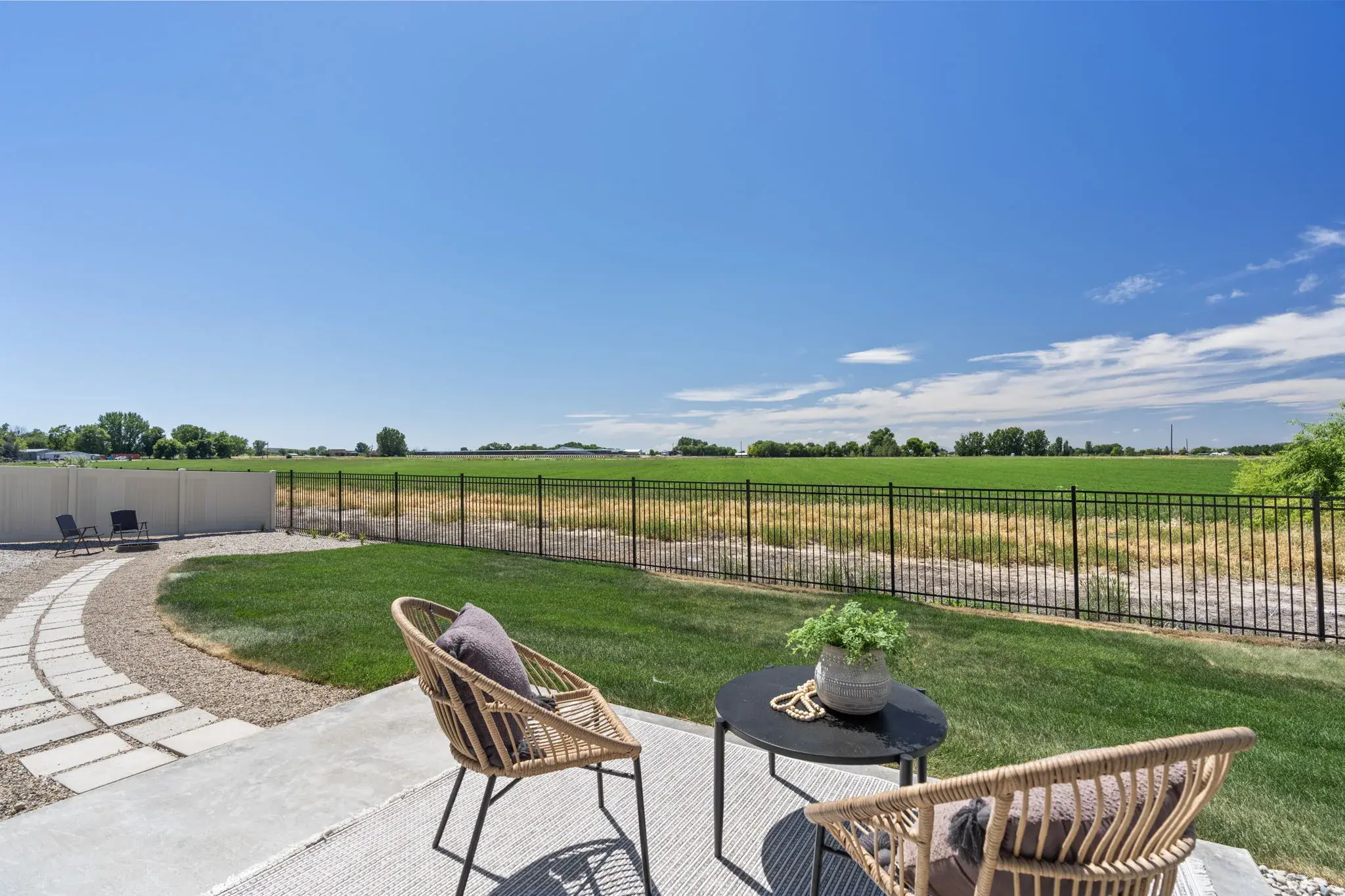 The back patio at Harvest Creek Vaulted Home: a concrete patio and lawn inside a black metal fence, with open farmland beyond
