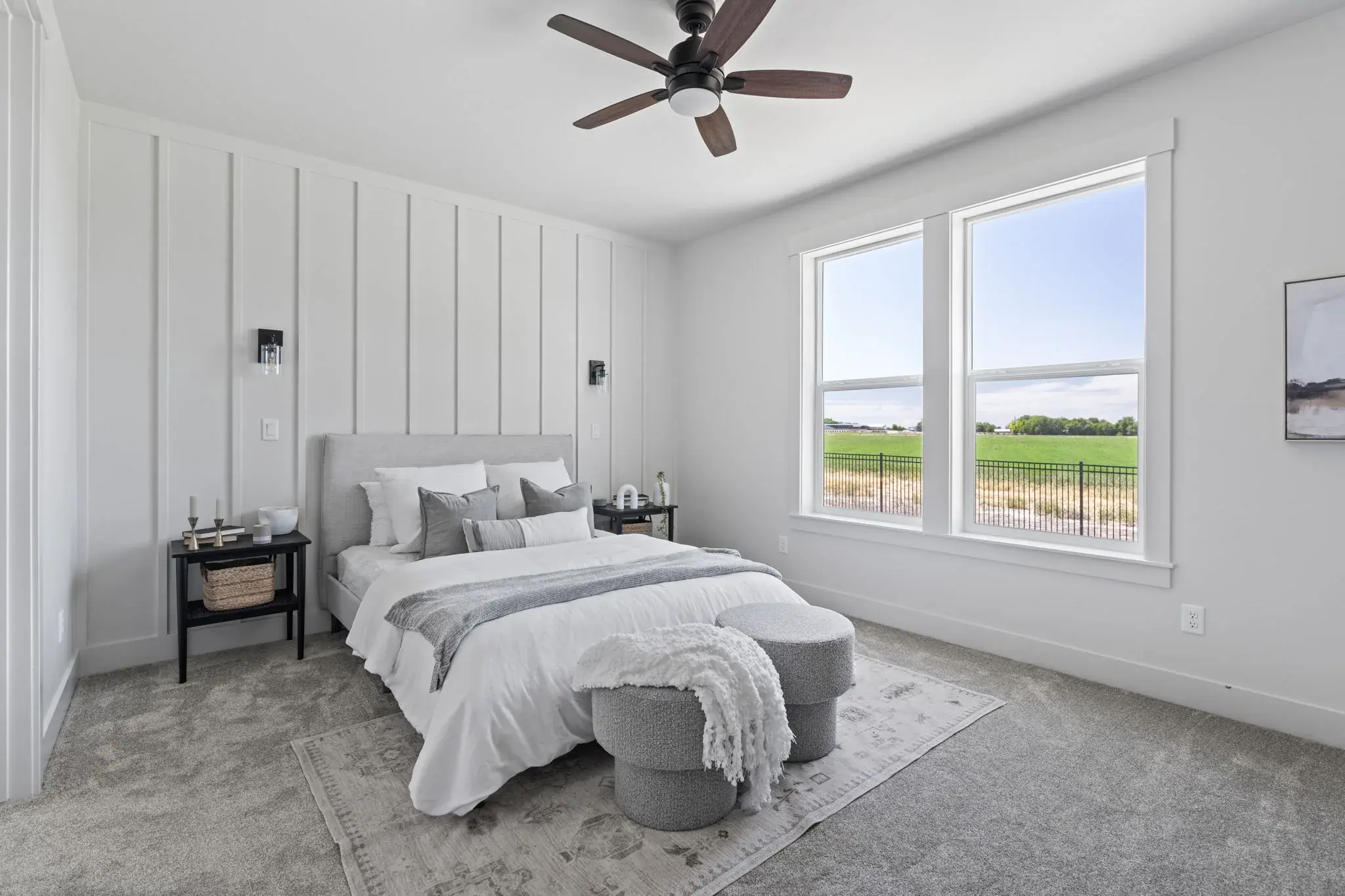 The primary bedroom at Harvest Creek Vaulted Home, carpeted, with a board and batten accent wall, wall sconces and windows onto the fields behind