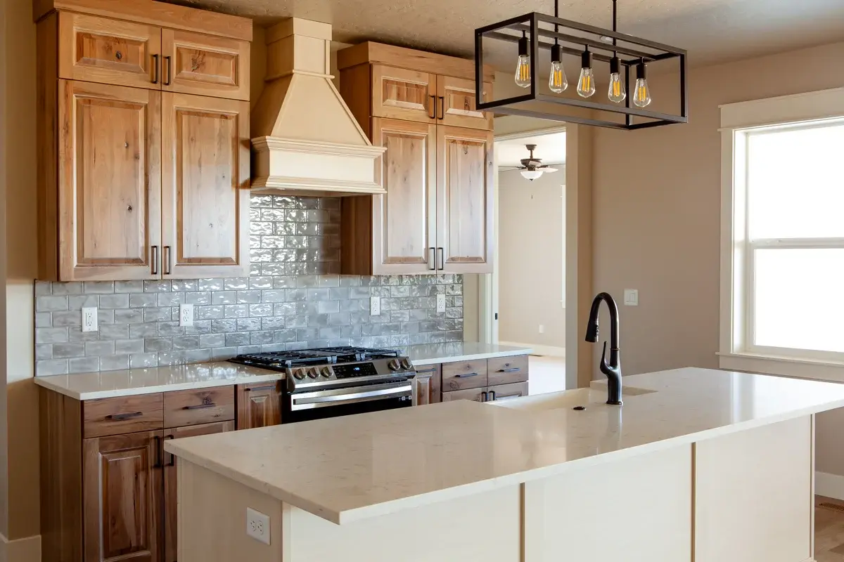 Kitchen with knotty hickory cabinets, gray tile backsplash, quartz island and black metal light fixture in a Bear Homes build