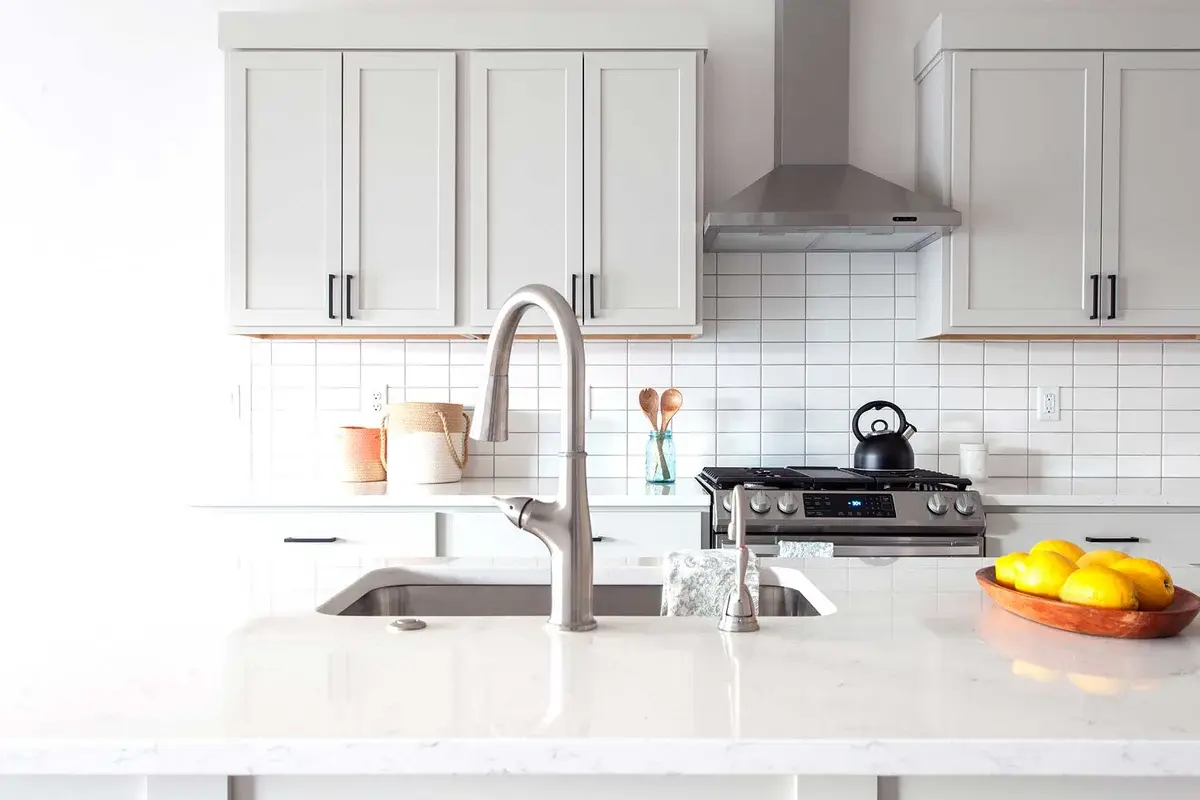 Bright kitchen with white shaker cabinets, white tile backsplash and a stainless range hood in a Bear Homes build
